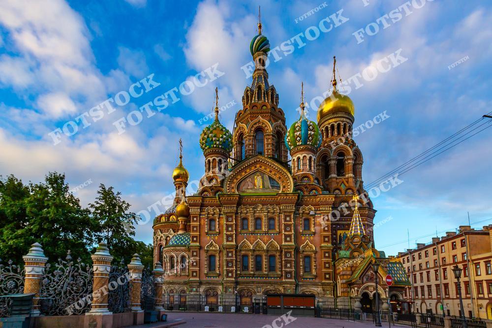 На фотографии запечатлен Храм Спас-на-Крови, один из самых знаковых памятников Санкт-Петербурга. Яркие купола, украшенные мозаикой, сверкают в лучах утреннего солнца. Фасад храма с изысканным орнаментом и деталями подчеркивает богатую историю этого места. Синий небосвод и окружающая зелень добавляют композиции гармонии.
